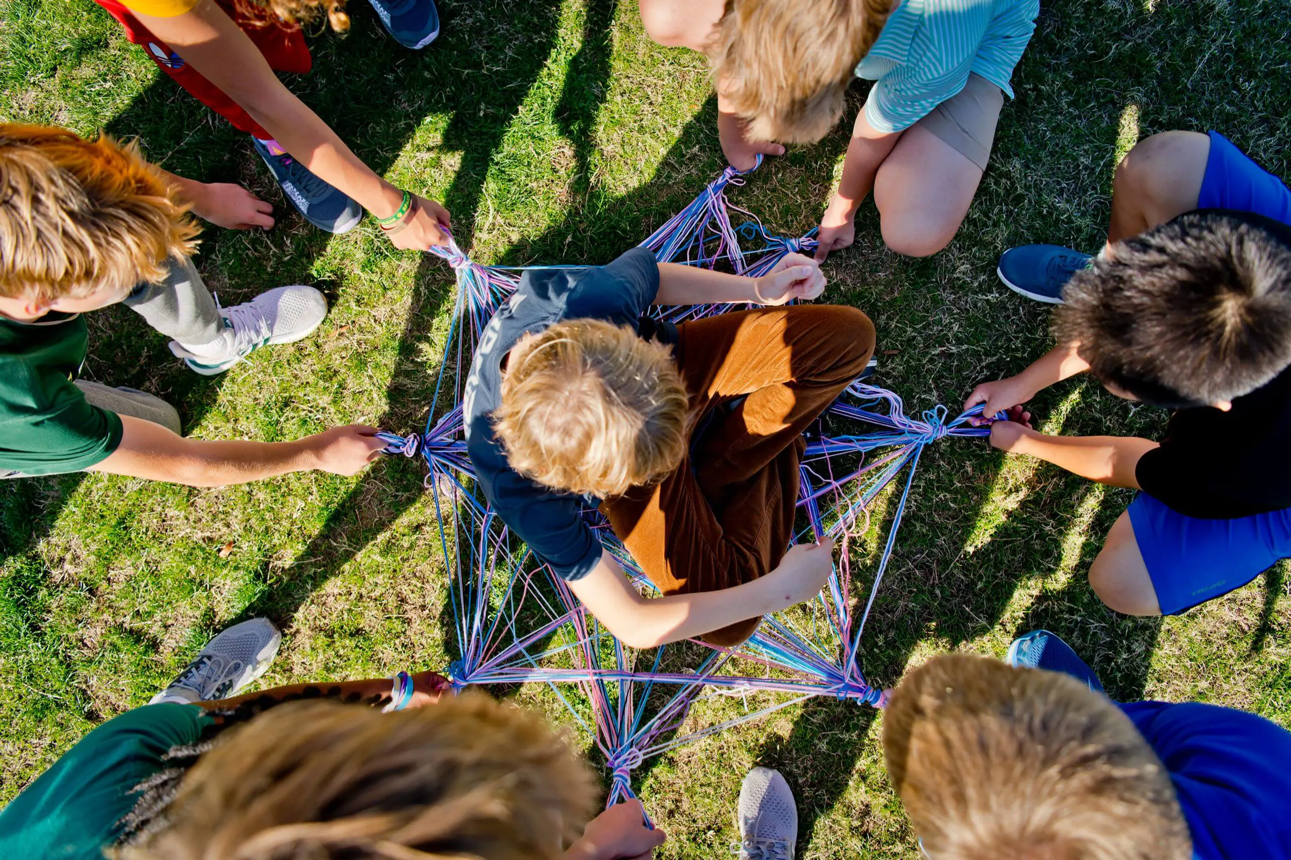 students working together outdoors on a team-building activity with ropes.